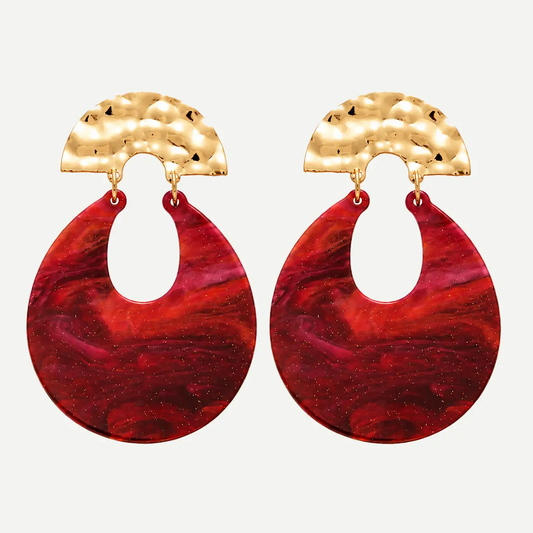 A pair of statement dangle earrings featuring textured hammered gold semi-circular tops and large teardrop-shaped red and magenta marbled resin drops, shown against a light gray background.